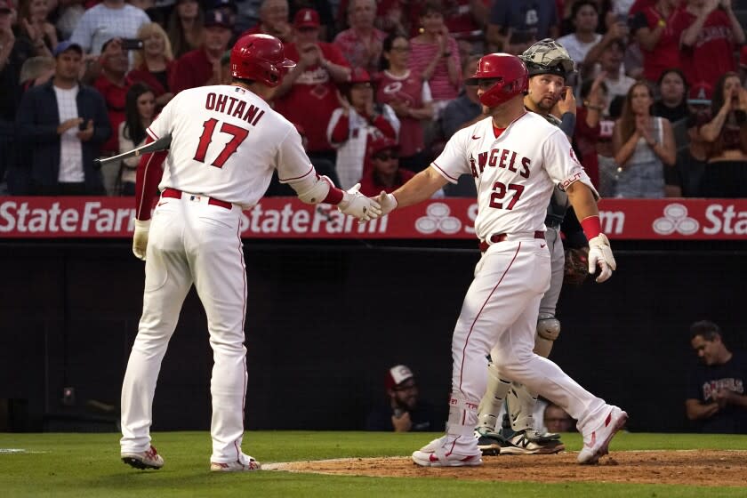 Los Angeles Angels' Mike Trout, center, is congratulated by Shohei Ohtani, left, after hitting a solo home run as Seattle Mariners catcher Cal Raleigh stands at the plate during the fourth inning of a baseball game Friday, June 24, 2022, in Anaheim, Calif. (AP Photo/Mark J. Terrill)